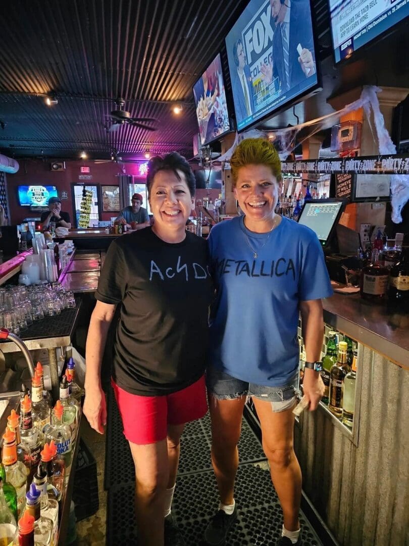 Two women standing in a bar with drinks on the counter.